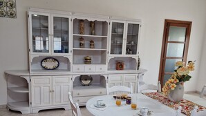 A dining area with a white table set for four, surrounded by white chairs. A white cabinet with glass doors is against the wall, and a vase with flowers is on the table. - Holiday Home Piscinas (SU)
Nice apartment a few kilometers from the sea (Piscinas)