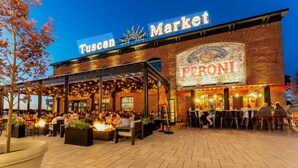 Un área de estar al aire libre con mesas y sillas, un letrero del Mercado de la Toscana y un letrero de cerveza Peroni.
