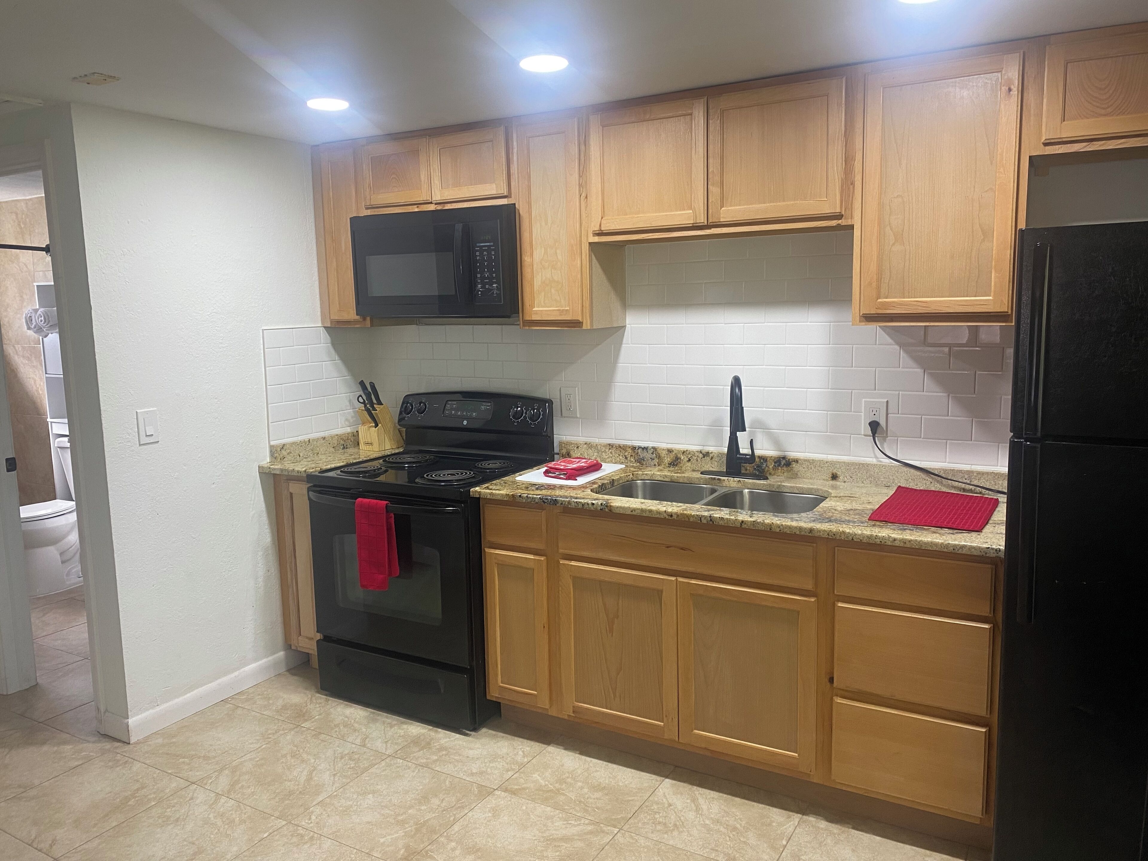 A kitchen with wooden cabinets, a black stove, a microwave, a sink, and a refrigerator.