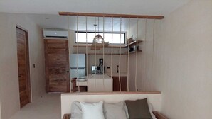 A bedroom with a wooden bed, a kitchen area in the background, and a hanging light fixture. - Magic jungle apartment in Tulum (Tulum)
