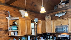 A kitchen with wooden cabinets, a granite countertop, a stainless steel oven, and a microwave. There are two bar stools and a hanging light fixture. - #1 Top-Rated Waterfront Lodge on Lake Fork Pet Friendly (Alba)