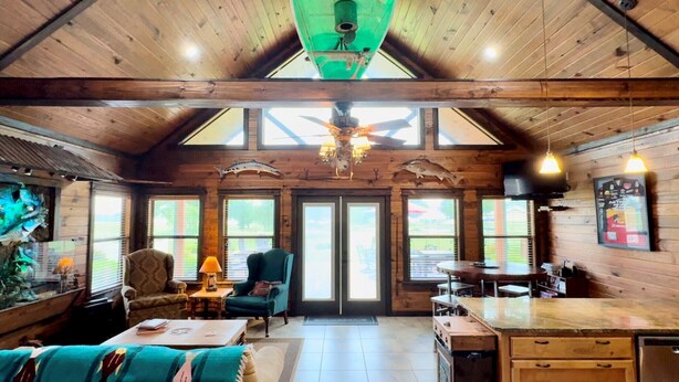 A rustic cabin interior with a high ceiling, wooden walls, a dining area, and a large window overlooking a scenic view. - #1 Top-Rated Waterfront Lodge on Lake Fork Pet Friendly (Alba)