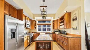 Una cocina con armarios de madera, un refrigerador de acero inoxidable, una isla central con espacio para vinos y un ventanal grande.