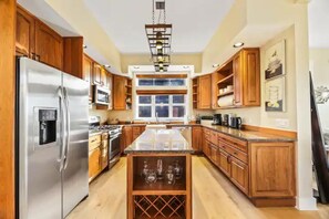 Una cucina con mobili in legno, un frigorifero in acciaio inossidabile, un'isola centrale con portabottiglie per vino e un'ampia finestra.