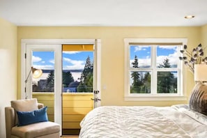Una camera da letto con un letto, una sedia, una lampada e una finestra vista alberi e un edificio.