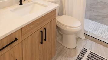Ein modernes Badezimmer mit einem weißen Waschtisch, schwarzen Wasserhähnen, einer Toilette und einer Dusche mit weißem Vorhang.