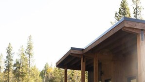 Eine moderne Holzblockhütte mit überdachter Veranda und großen Fenstern, umgeben von einem Wald.