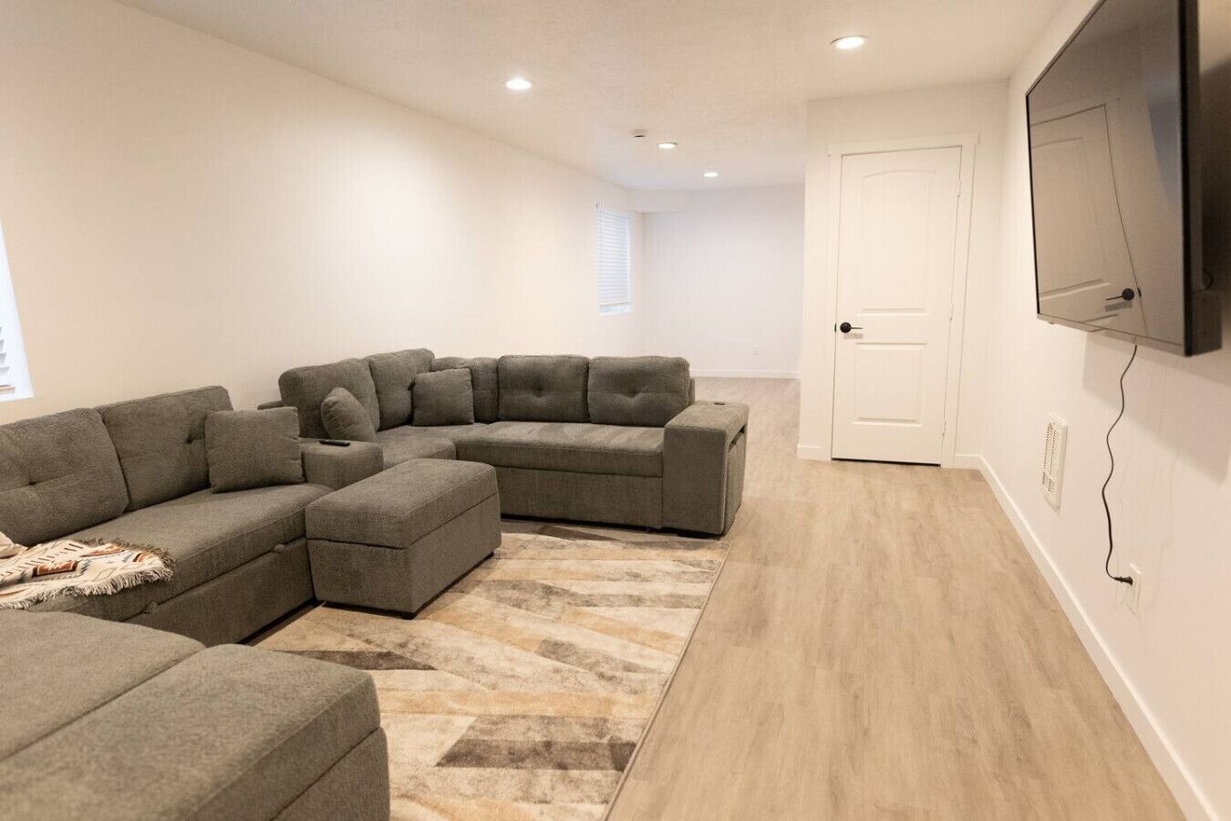 Un salon moderne avec un canapé d’angle, un petit pouf et un tapis à motifs.
