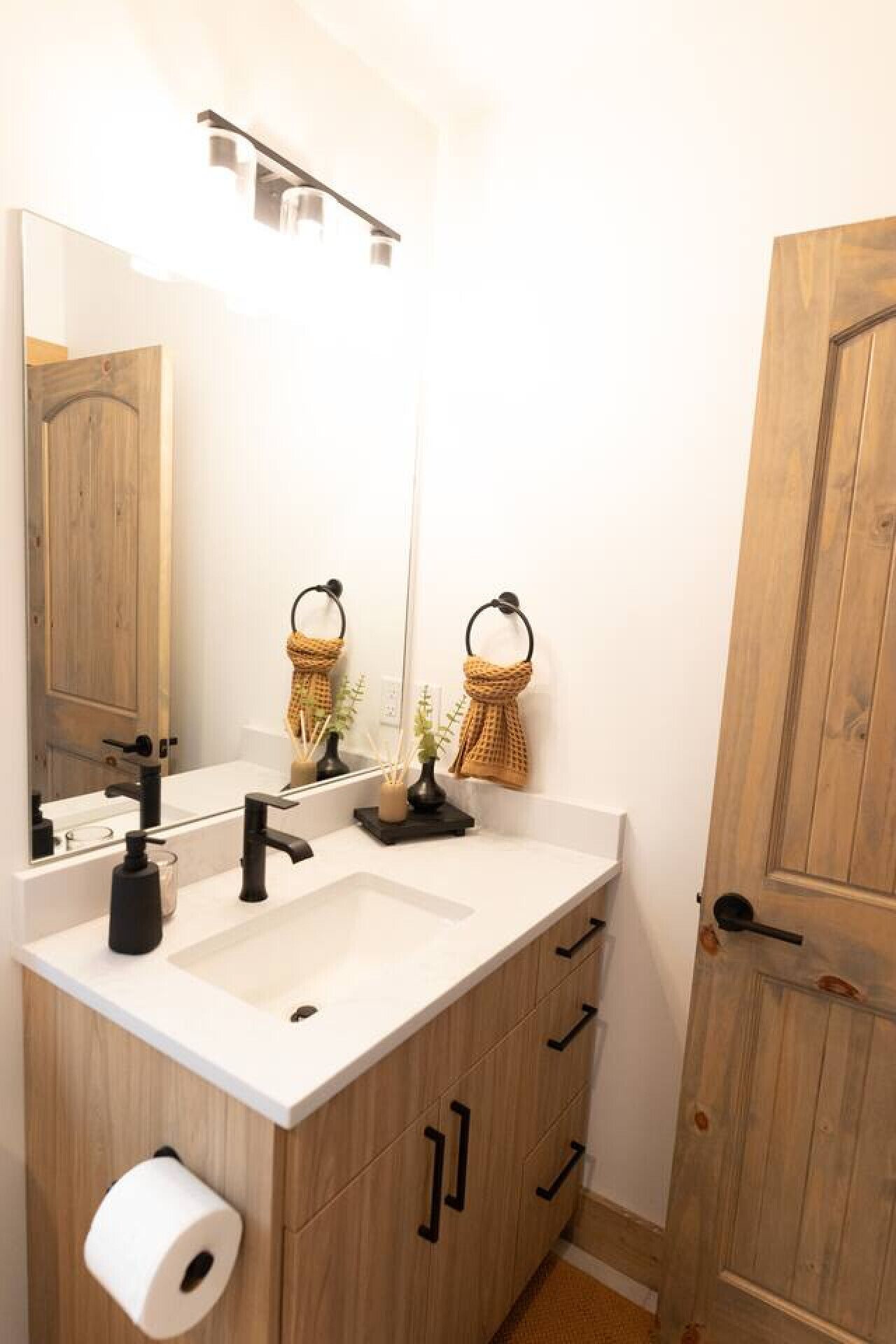 Een badkamer met een grote spiegel, twee wastafels, houten kastjes, een handdoekrek en een deur.