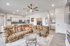 A spacious living area with a sofa set, a glass coffee table, and a ceiling fan.