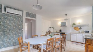 A dining area with a round table and wooden chairs, a kitchen with white cabinets, and a patterned wall. - Gîte La Terrasse, near CNPE and Via Rhôna, ideal for cycling enthusiasts! (Lagnieu)