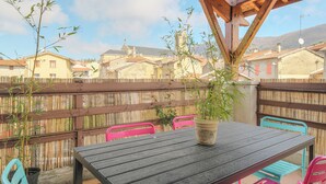 A wooden table with a potted plant, surrounded by pink and turquoise chairs, under a wooden pergola. - Gîte La Terrasse, near CNPE and Via Rhôna, ideal for cycling enthusiasts! (Lagnieu)