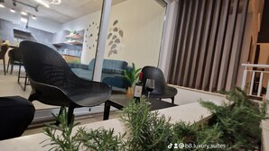 A modern indoor seating area with black chairs and a table, a clock on the wall, and a potted plant.