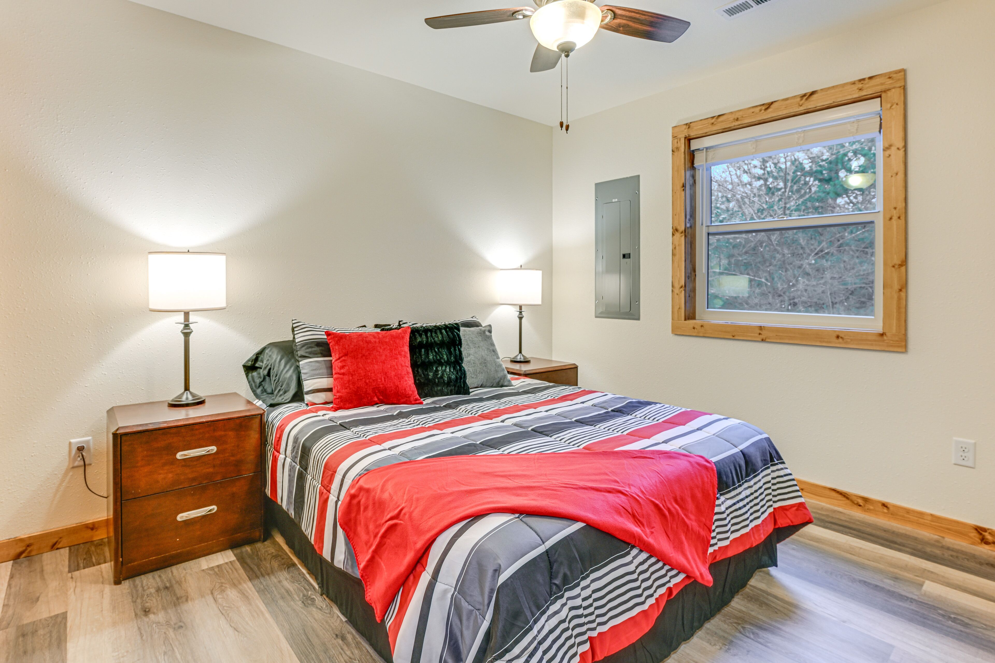 A bedroom with a bed, two bedside tables, two lamps, a ceiling fan, a window, and a wooden floor.