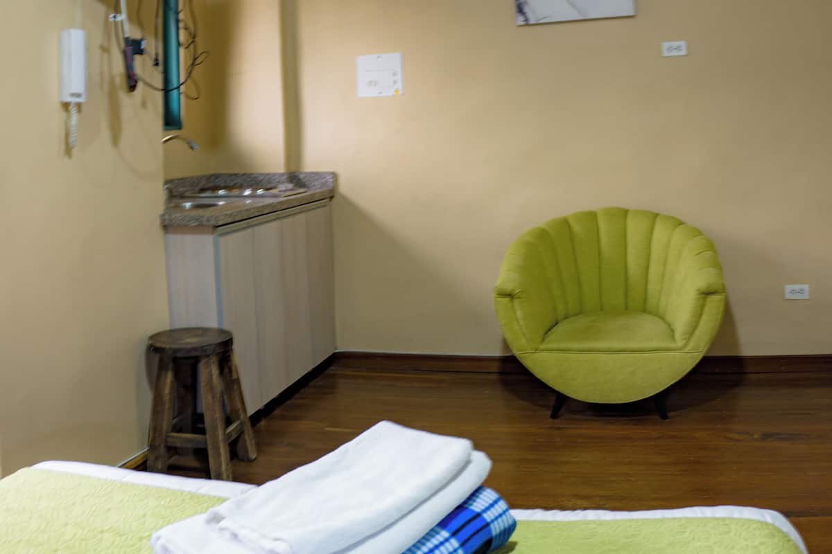 A room with a bed, a green armchair, a television mounted on the wall, and a painting.