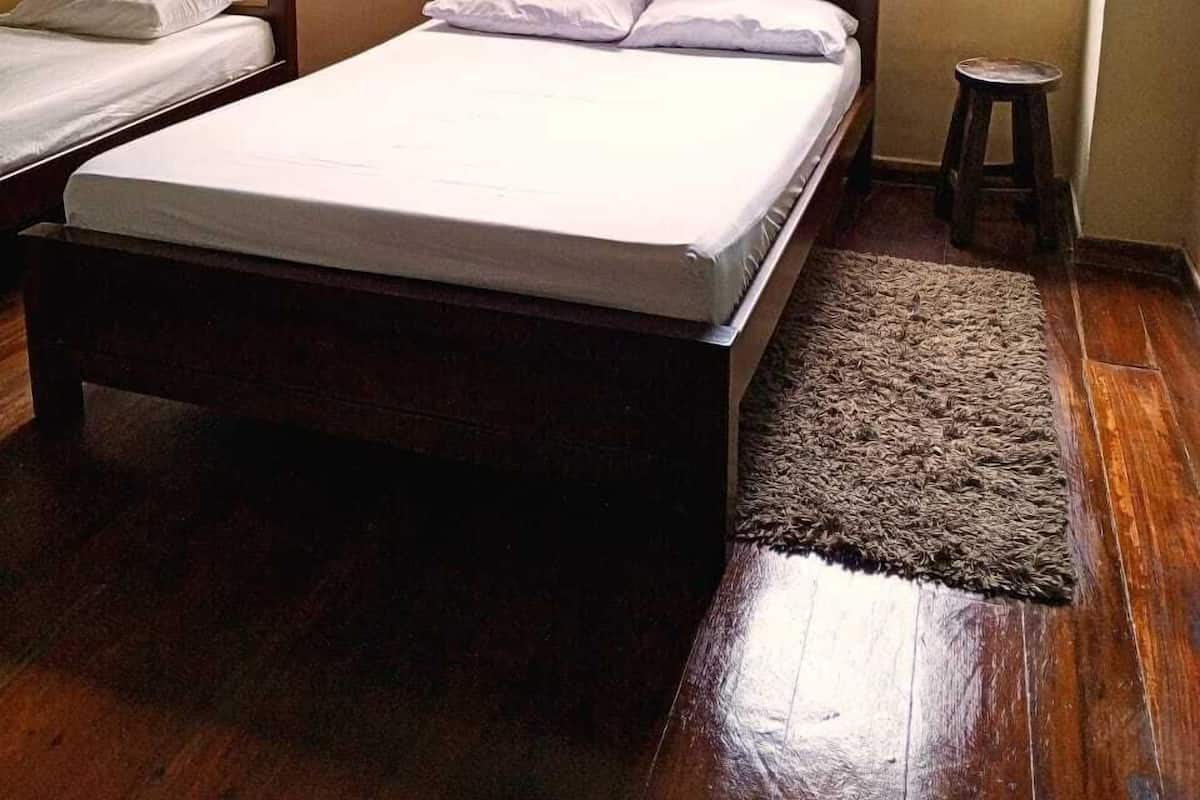 A room with a single bed, a bunk bed, a small stool, and a window with a view of greenery.