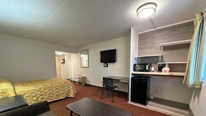 A compact hotel room with a bed, a small desk, a chair, a microwave, and a television. - THE INN- PITTSBURGH (Pittsburgh)