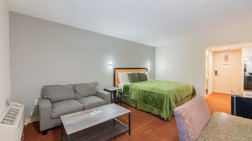 A hotel room with a bed, a sofa, a small table, and a heater.