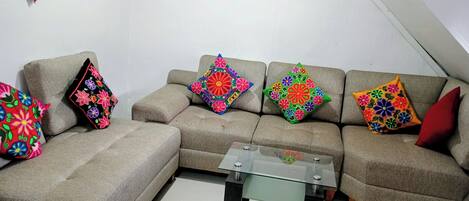 A living room with a beige sectional sofa, colorful floral cushions, and a glass-top coffee table.