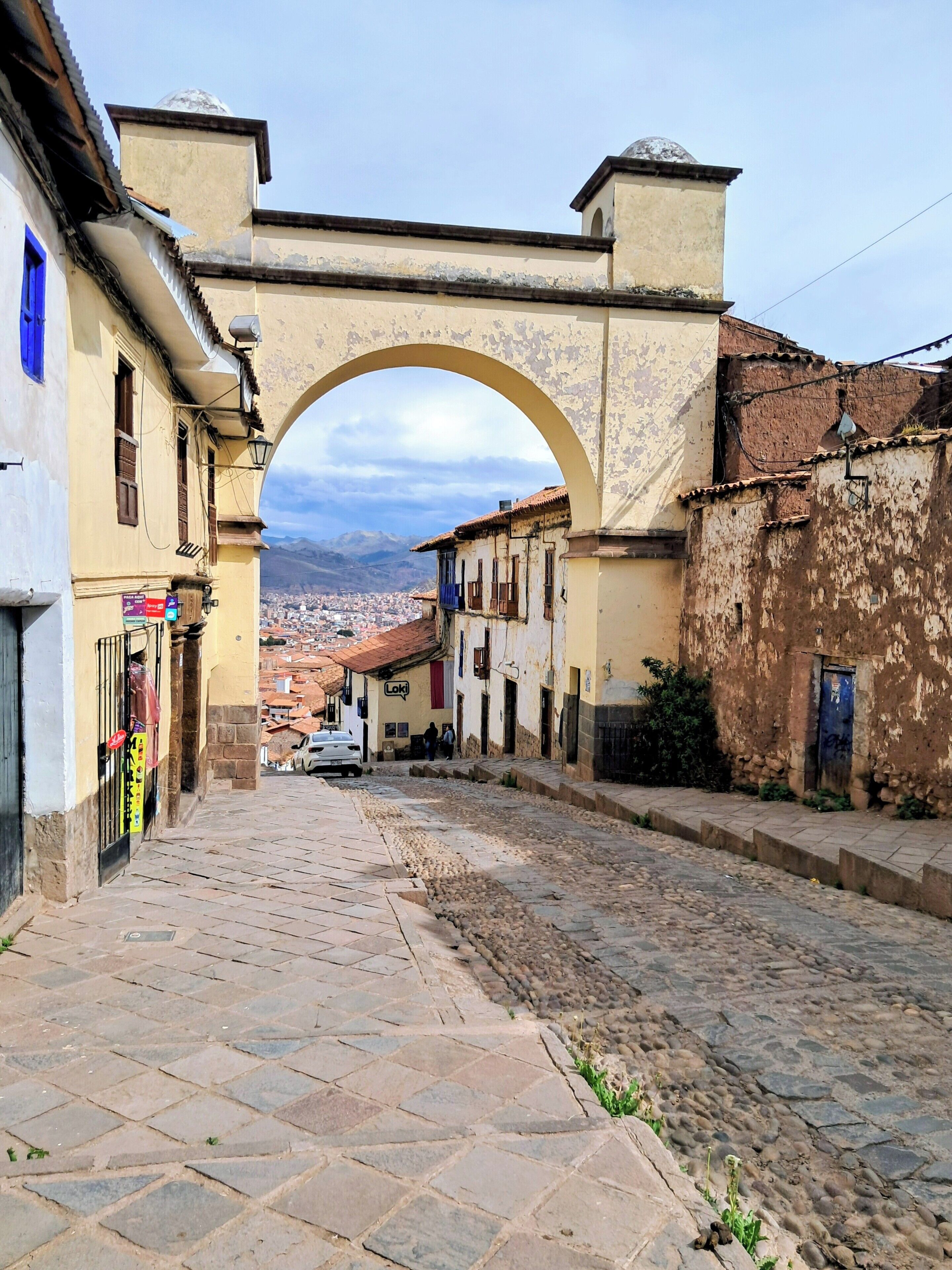 A cobblestone street leading through an arched gateway with buildings on either side.