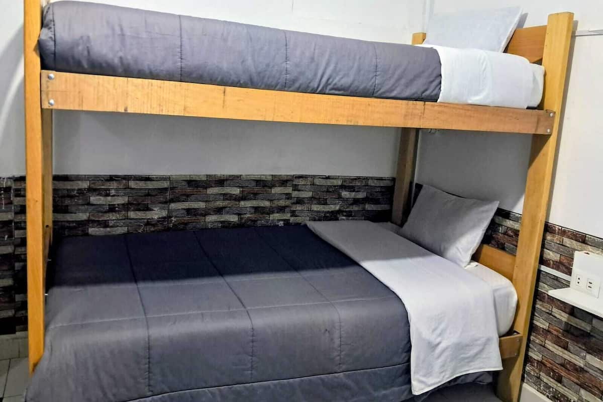 Un lit superposé avec une literie grise, une structure en bois et un mur décoré d’un motif imitant la pierre.
