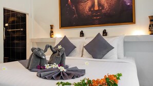 Habitación de hotel con una cama bien hecha, un cuadro grande de Buda sobre la cama y una zona de ducha con pared de azulejos negros.