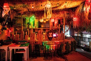 A bar area with wooden furniture, a thatched roof, and various bottles and decorations. - Bungalow - Sleeps 2 - Terrace - Beach Close (Ko Lanta)