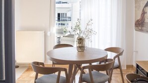 Ein Essbereich mit einem runden Holztisch, sechs Stühlen, einer Hängeleuchte und Blick auf einen Balkon mit Sitzmöbeln.