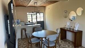 Comedor con una mesa redonda y cuatro sillas, zona de bar con mostrador y taburetes, y una cocina visible al fondo.