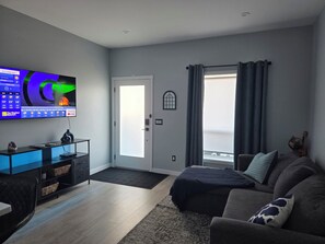 Una sala de estar moderna con una televisión de pantalla plana, un sofá, una mesa de centro y una puerta que da a un balcón.