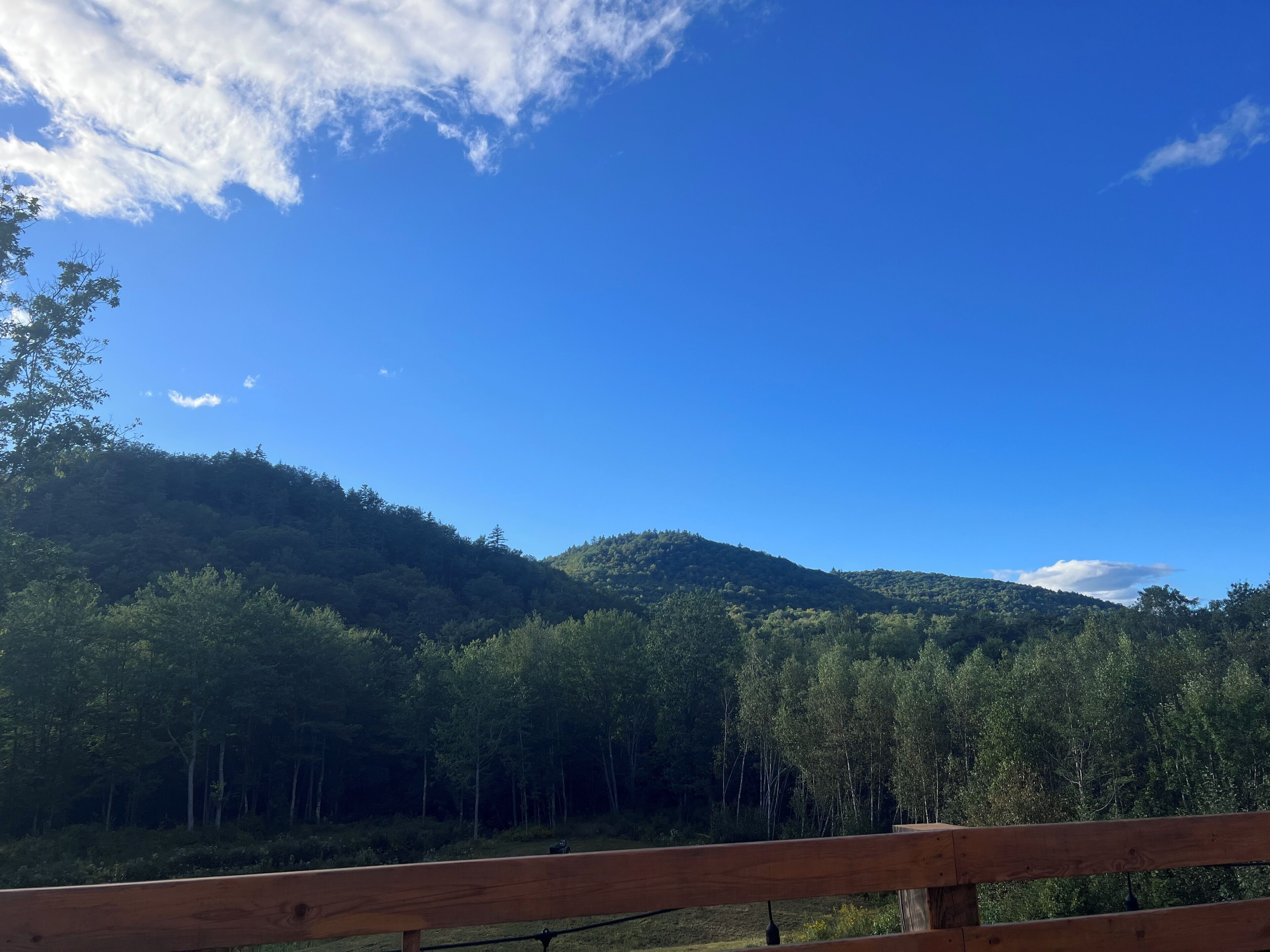 A wooden deck with a view of a forested mountain under a clear blue sky.