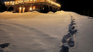A wooden cabin with a covered porch, surrounded by snow, under a night sky with a visible moon. - Experience Bethel charm near Sunday River  (Bethel)