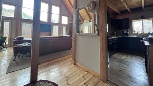 A spacious living room with a large window, a wooden ceiling, and a cozy seating area. - Experience Bethel charm near Sunday River  (Bethel)