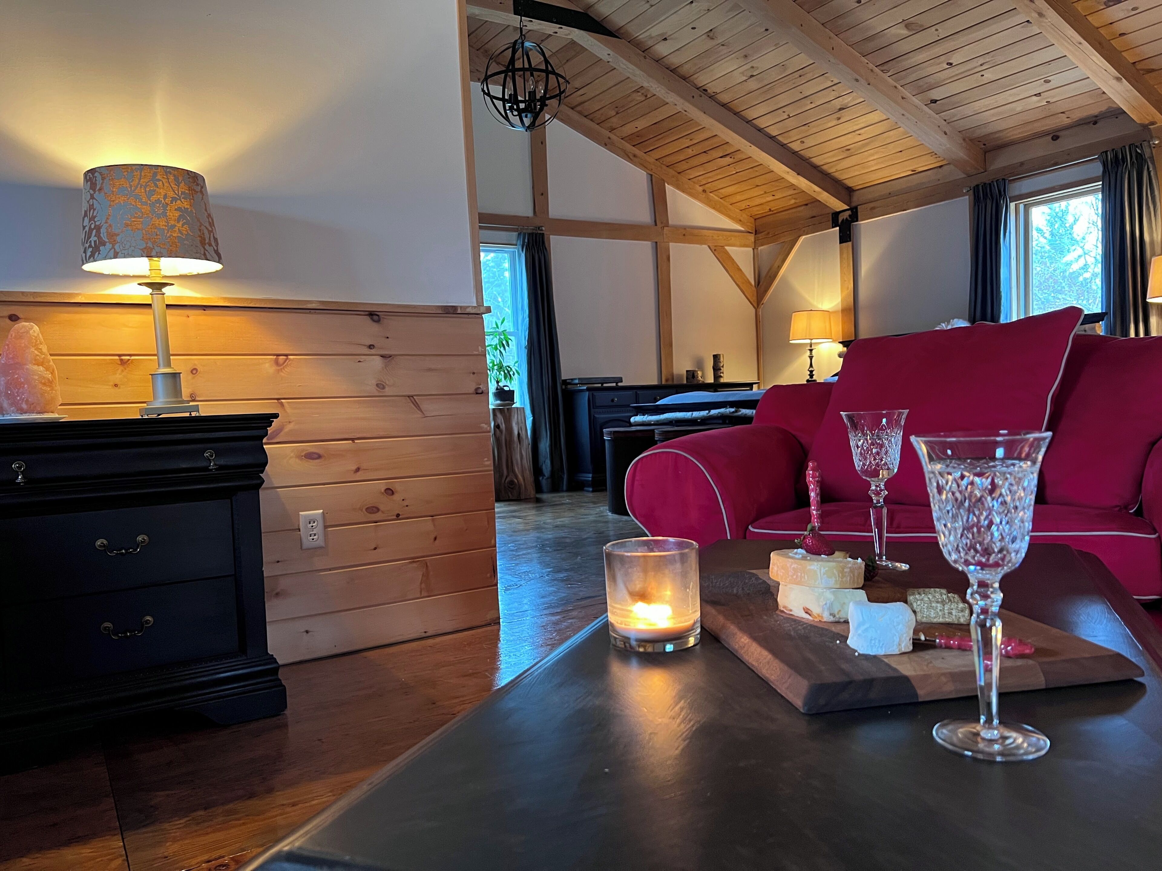 Una habitación acogedora con techo de madera, un sofá rojo, una mesa con velas y una lámpara.