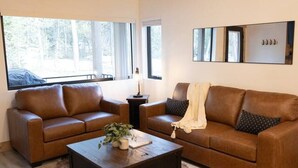 Un salon moderne avec un canapé en cuir marron, une table basse en bois et une grande fenêtre laissant entrer la lumière naturelle.