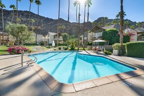 A swimming pool with a clear blue water, surrounded by palm trees and a mountain backdrop.