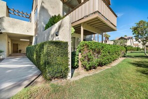 A modern two-story residential building with a concrete facade, a balcony, and a well-maintained garden.