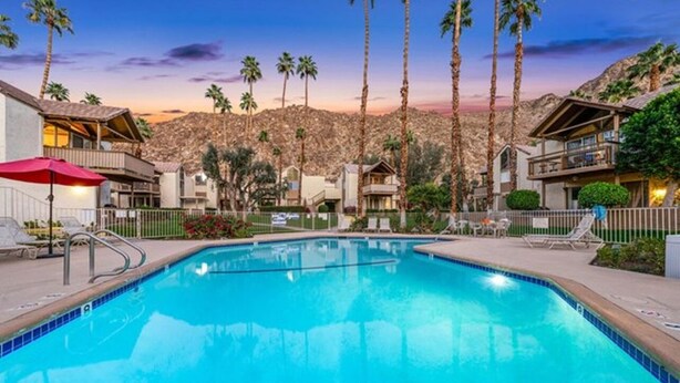 A swimming pool with lounge chairs and umbrellas, surrounded by buildings and palm trees. - Condo paradise in Indian Wells. (Indian Wells)