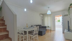 Moderni olohuone, jossa on ruokailutila, harmaa sohva, pieni pöytä, jossa on kasvi, ja portaat, jotka johtavat ylempään kerrokseen.