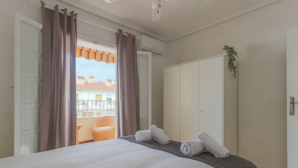 Hotellihuone, jossa on suuri sänky, vaatekaappi ja parveke, jolta on näkymä rakennuksiin.