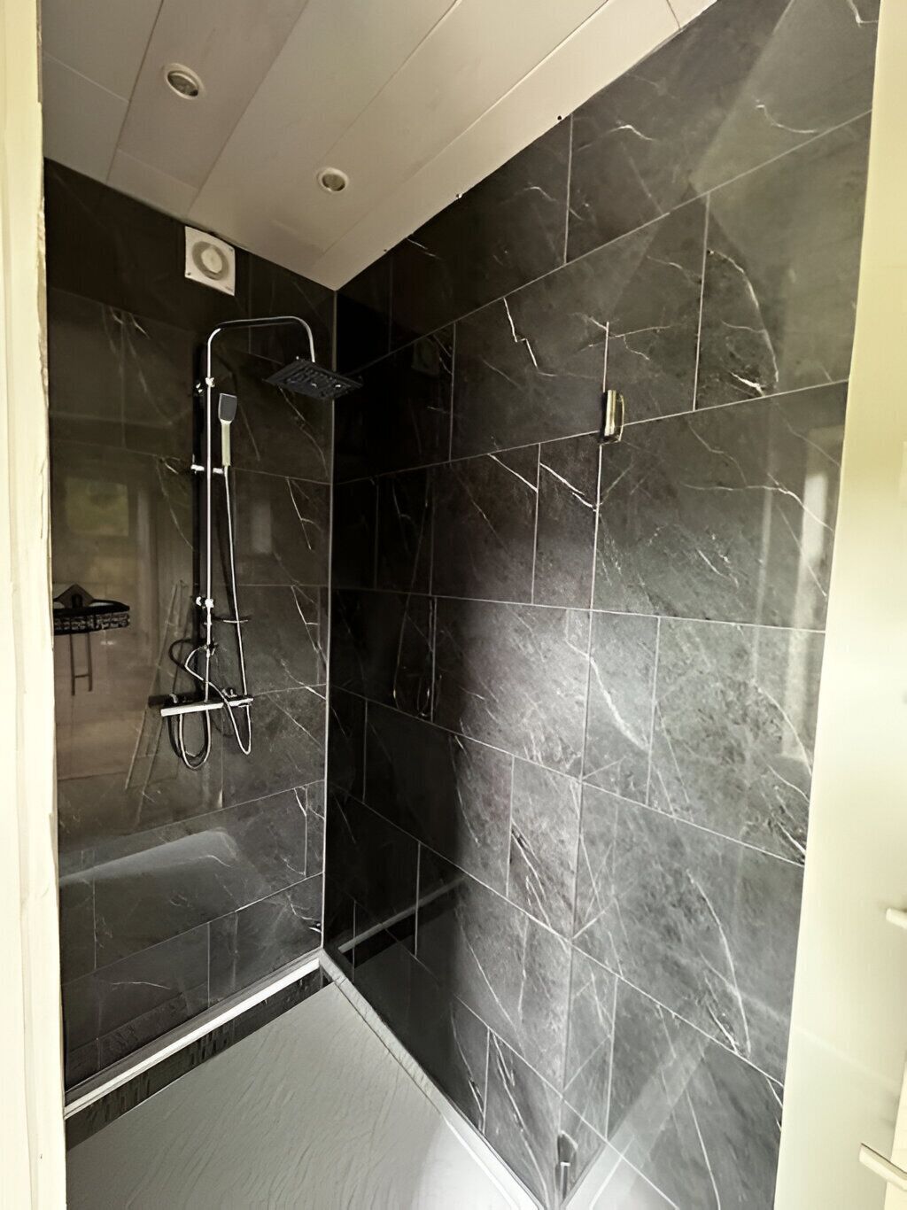 Ein modernes Badezimmer mit dunklen Marmorfliesen, einer Duschkabine aus Glas und einer sichtbaren Toilette.