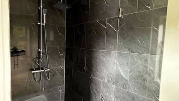 Ein modernes Badezimmer mit dunklen Marmorfliesen, einer Duschkabine aus Glas und einer sichtbaren Toilette.