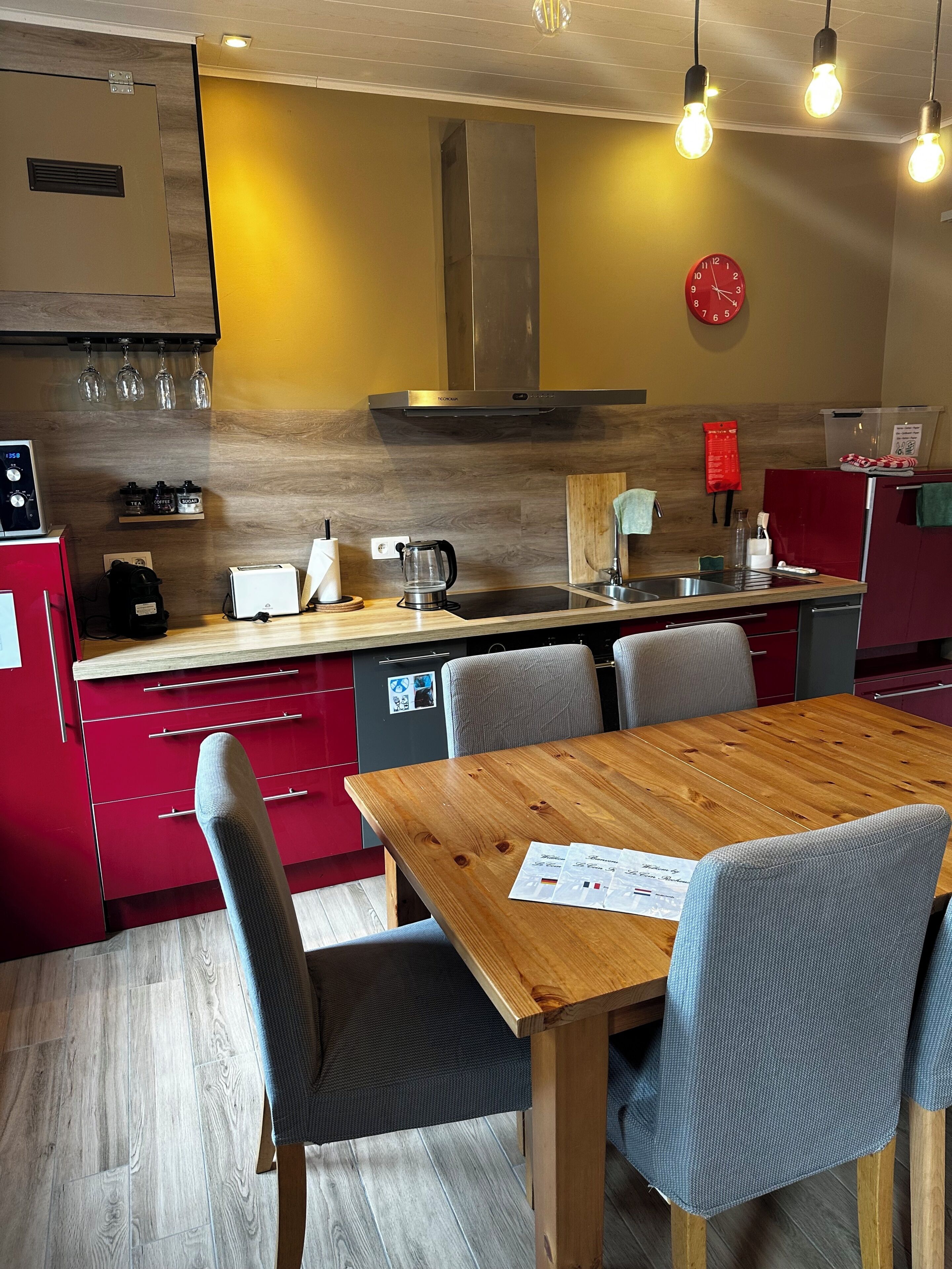 Eine moderne Küche mit einem Holztisch, Stühlen, einem roten Kühlschrank und einer Uhr an der Wand.
