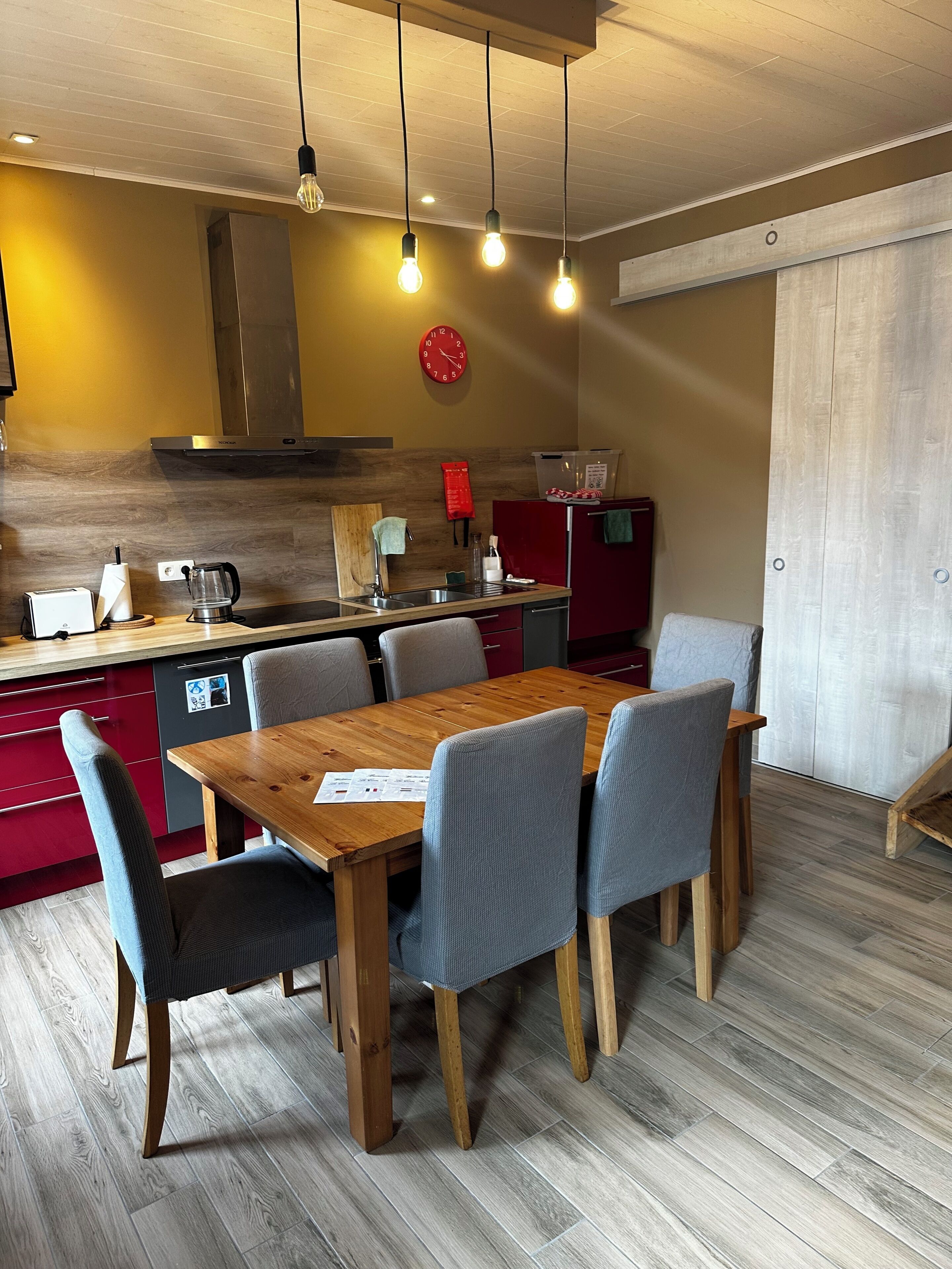 A modern kitchen with a wooden table, chairs, and a red refrigerator.
