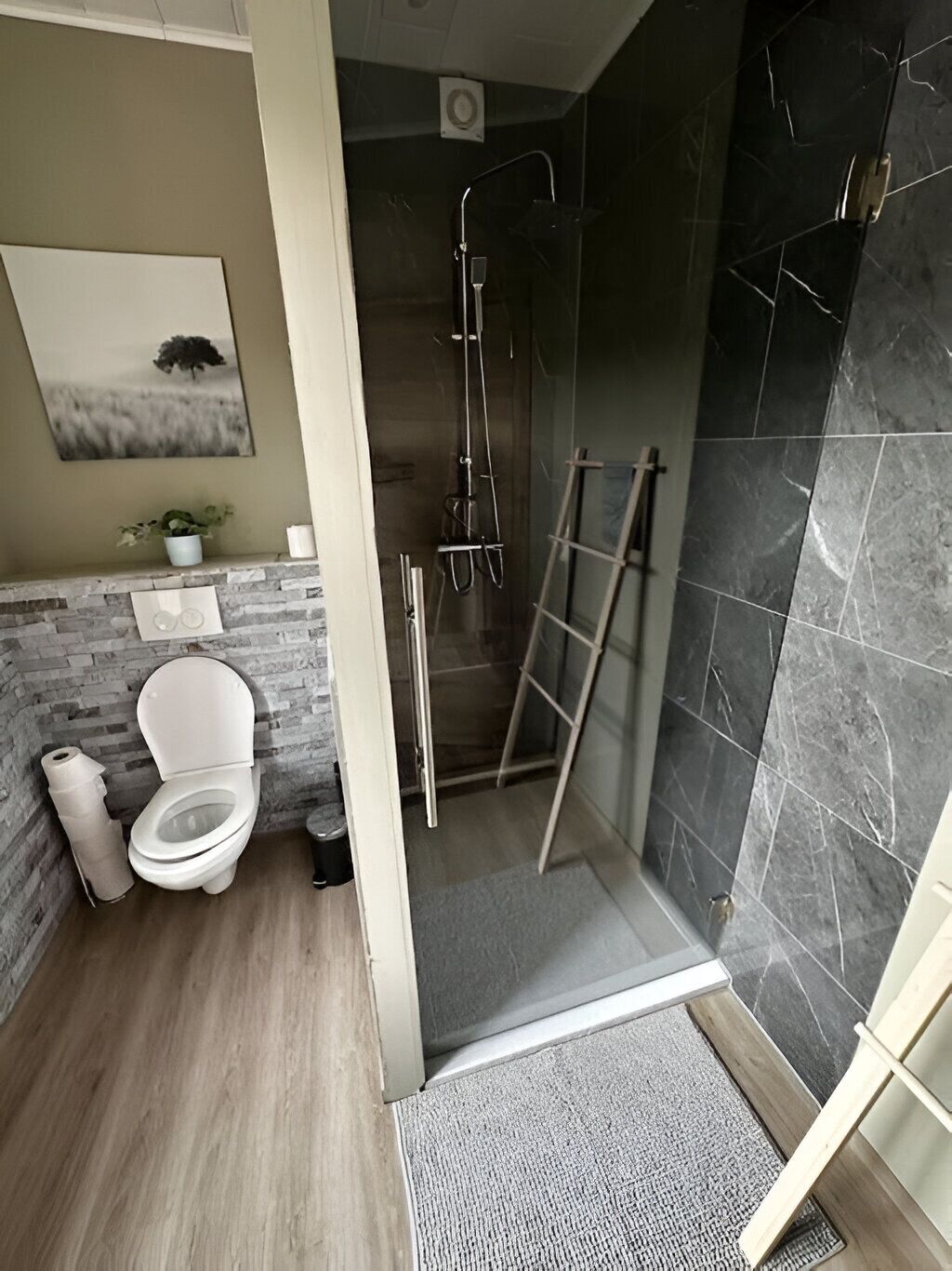 Un baño con inodoro, ducha y pared de mármol.