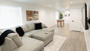A modern living room with a sectional sofa, a foosball table, and a flat-screen TV mounted on the wall. - NEW Mountain Modern Cabin (Unit 4) (Island Park)