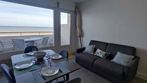 Een eetgedeelte met een tafel gedekt voor twee personen, een bank en uitzicht op het strand.