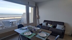 Een eetgedeelte met een tafel gedekt voor twee personen, een bank en uitzicht op het strand.