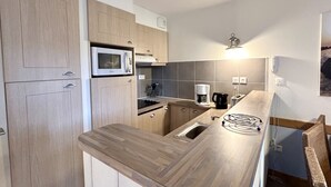 Eine kleine Küche mit Holzschränken, einer Mikrowelle, einer Kaffeemaschine und einem Spülbecken.