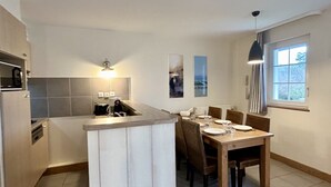 A modern kitchen with a dining area, featuring a central island, a built-in oven, and a window providing natural light.